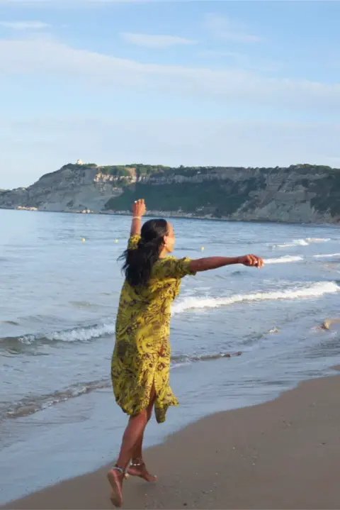 Dunja tanzt locker am Strand, im Hintergrund das Meer.