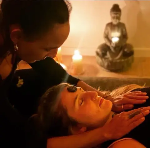 Reiki bei Kerzenlicht, Hände am Gesicht einer liegenden Frau.